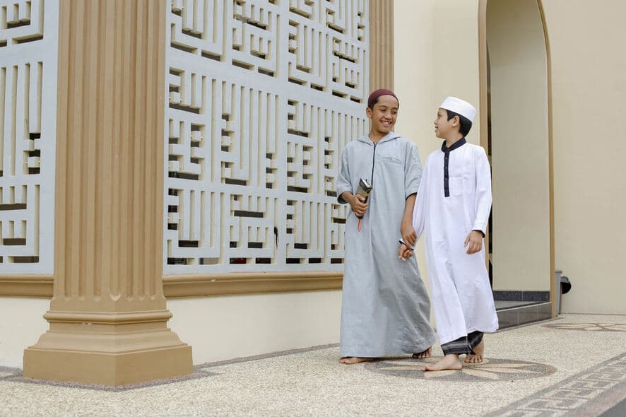 Two children walking past a mosque with happy expressions.